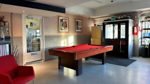 A pool table in a room with a red chair, a door with a sign, and a fire extinguisher. - Arkadia Hotel & Hostel (Helsinki)