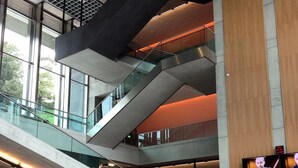 Un intérieur moderne à plusieurs niveaux, doté de rampes en verre et d’un espace d’accueil avec des écrans numériques.