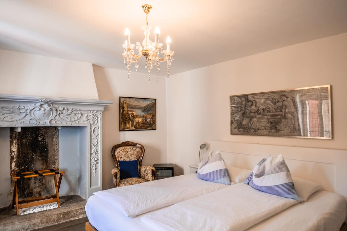 Un dormitorio con una cama grande, una chimenea, un candelabro y dos cuadros en la pared.