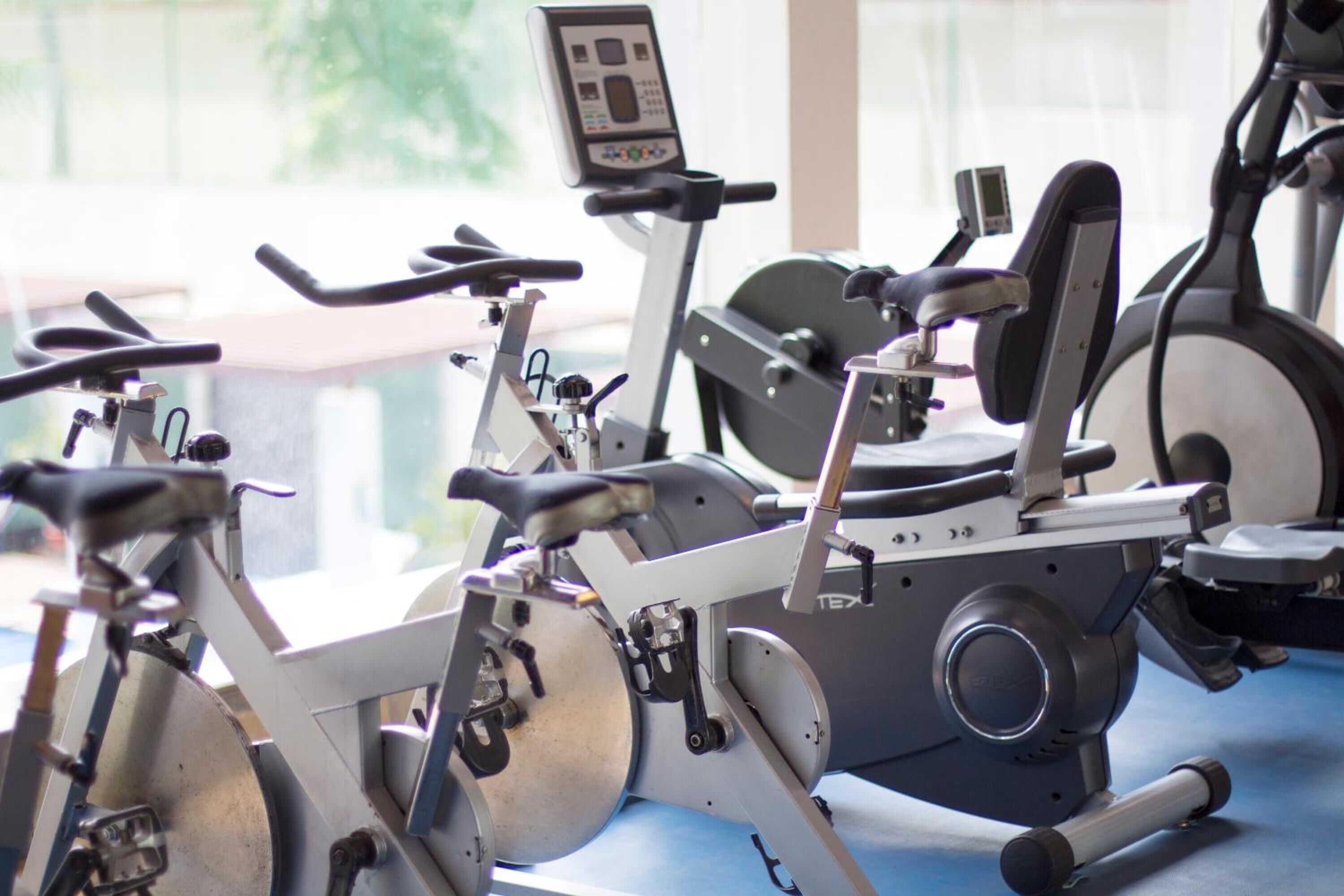 Varias bicicletas estáticas alineadas en un gimnasio, cada una con un panel de control.