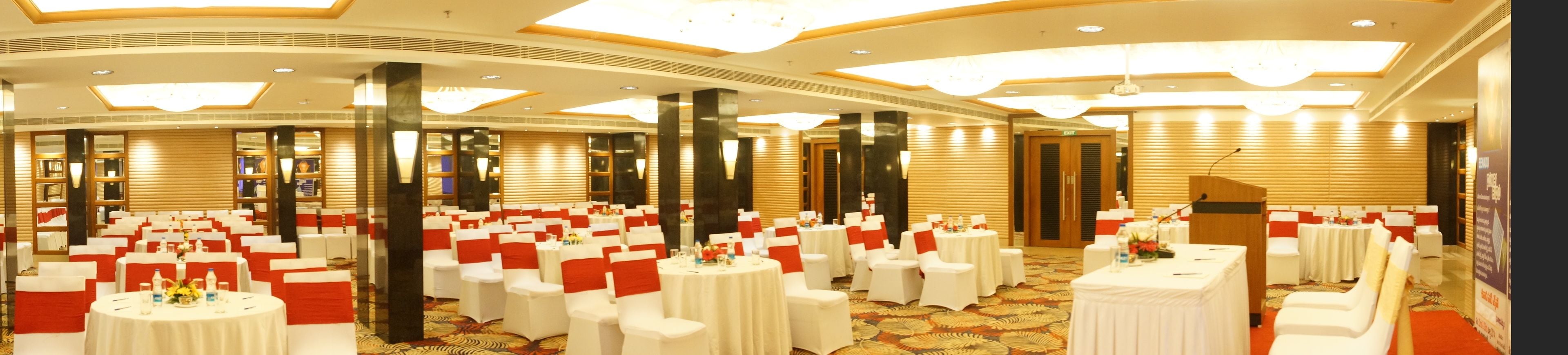 Une salle de banquet avec des tables rondes et des chaises, un podium et un grand lustre.