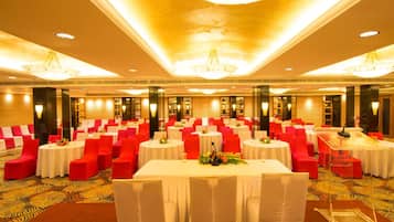 Un salón de banquetes con mesas redondas, sillas rojas y blancas, y candelabros.