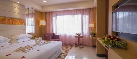 A hotel room with a large bed, a desk, a chair, a TV, and a window with curtains.