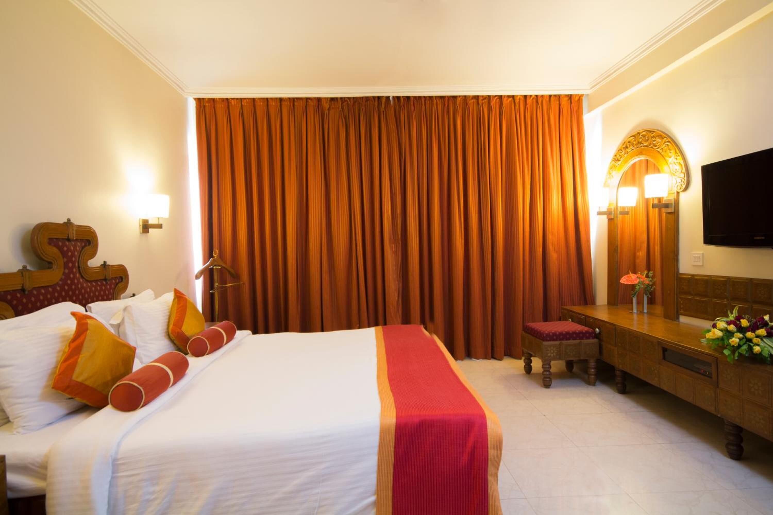 A hotel room with a large bed, a desk, a television, and a curtain.