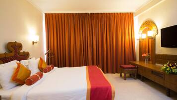 A hotel room with a large bed, a desk, a television, and a curtain.