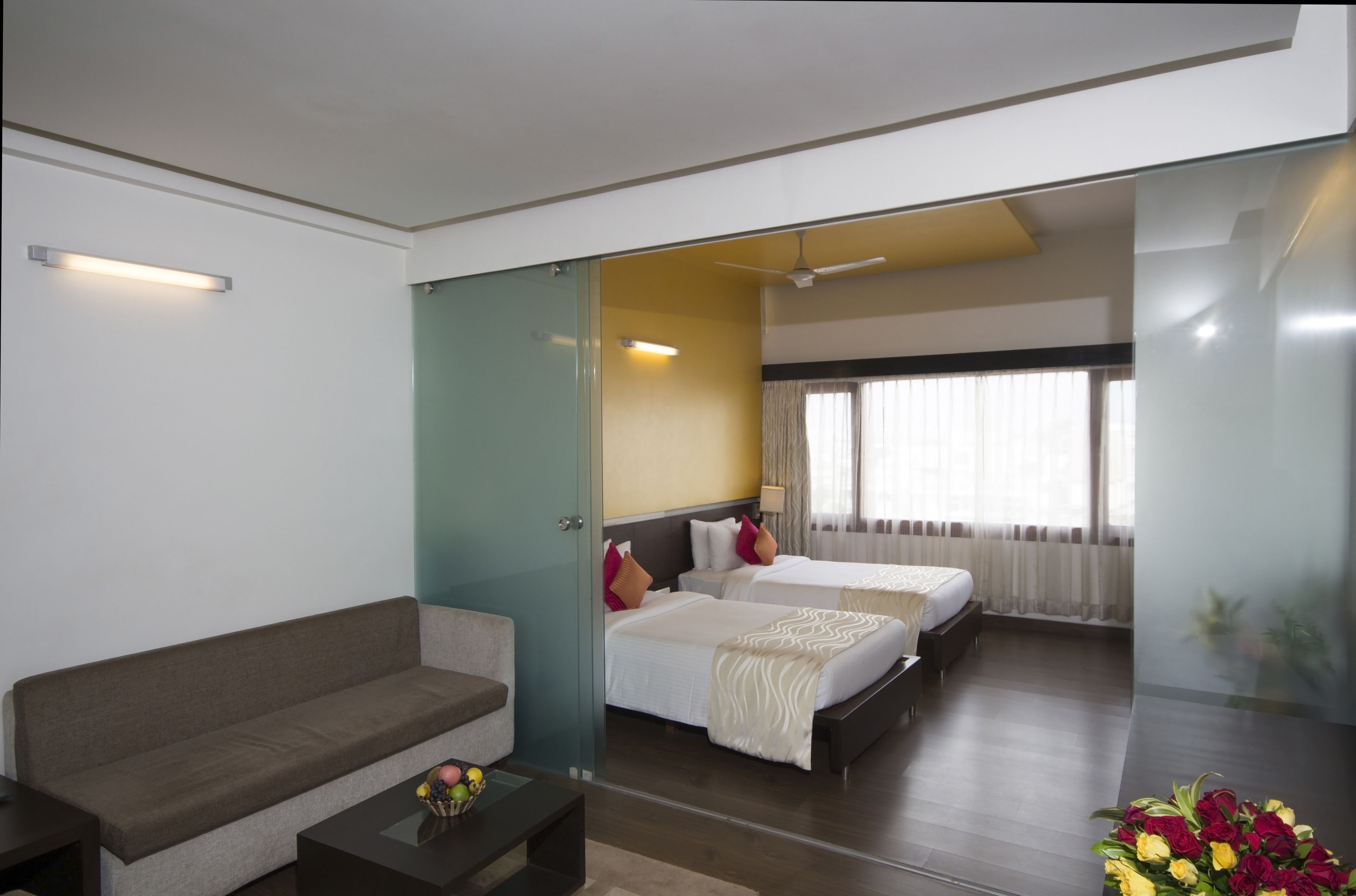 Une chambre d’hôtel avec un canapé, deux lits, une petite table avec des fruits et un bouquet de fleurs.