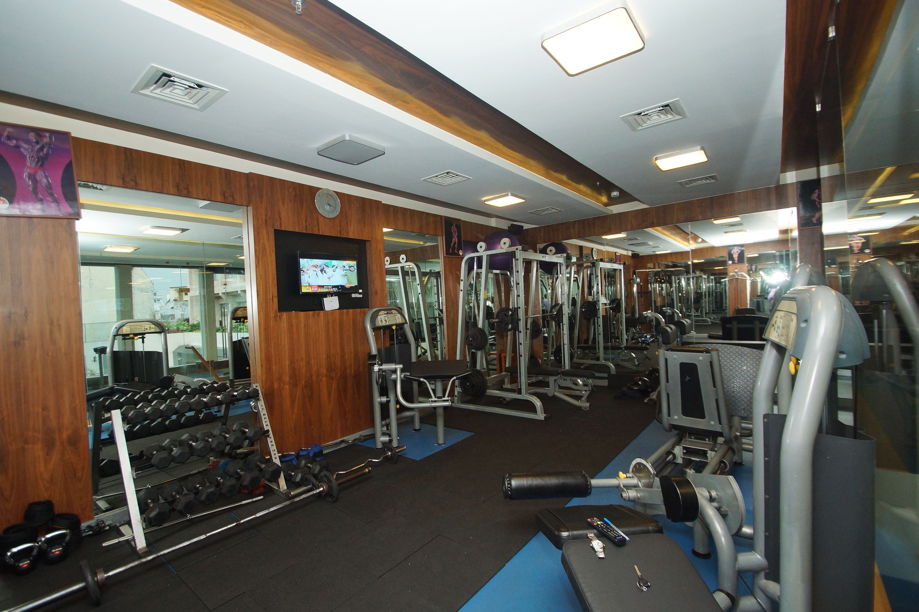 A gym with various exercise equipment, mirrors, and a television screen.