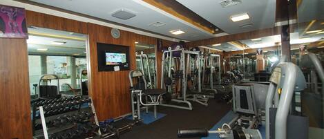 A gym with various exercise equipment, mirrors, and a television screen.