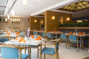 Un ristorante con tavoli apparecchiati, tovaglioli arancioni, sedie blu e centrotavola floreali.