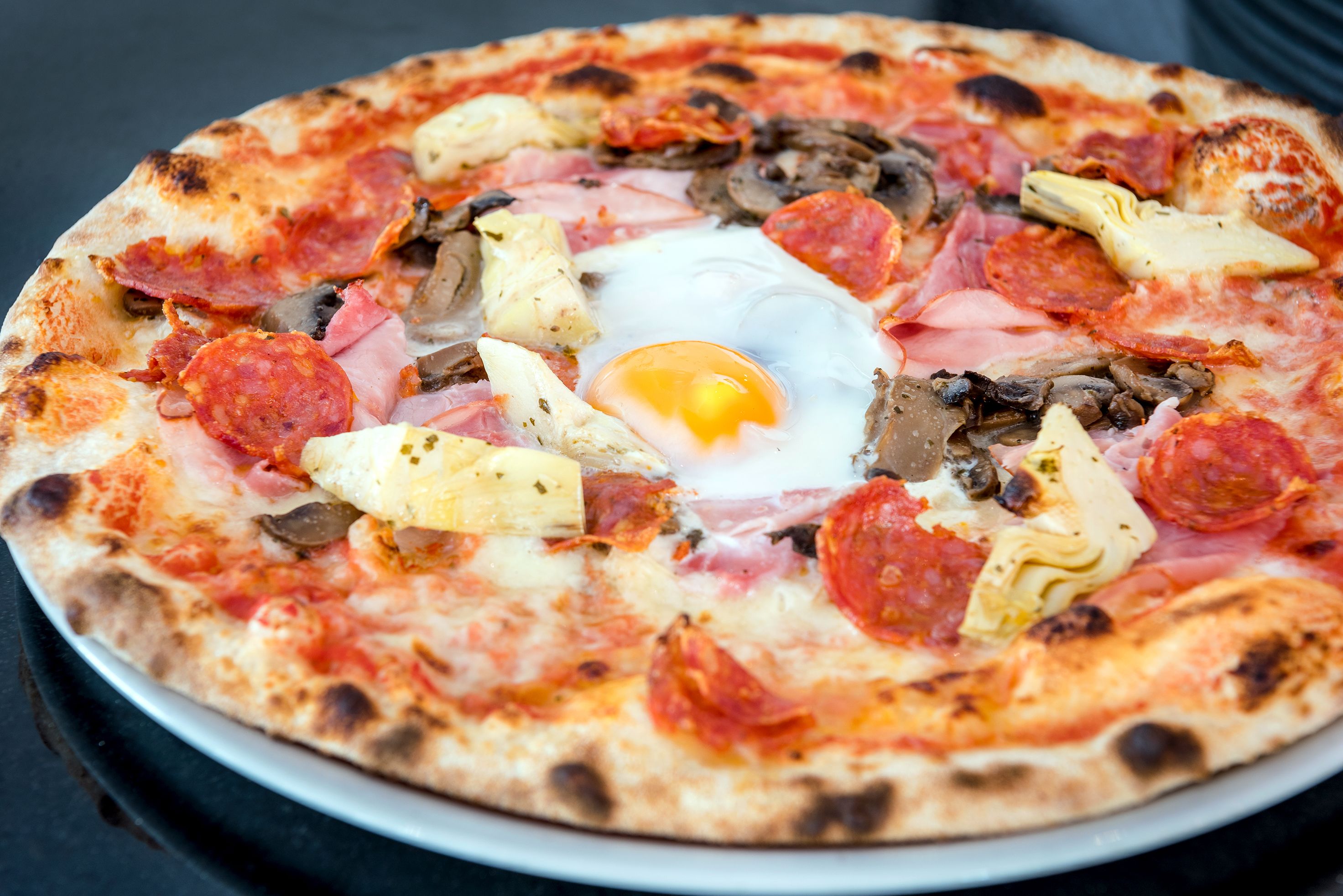 Pizza, jossa on erilaisia täytteitä, kuten kinkkua, sieniä ja paistettu kananmuna keskellä.