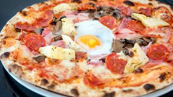 Pizza, jossa on erilaisia täytteitä, kuten kinkkua, sieniä ja paistettu kananmuna keskellä.