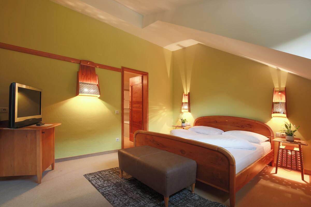 A bedroom with a wooden bed, bedside lamps, a television on a wooden cabinet, and a small table with a plant.