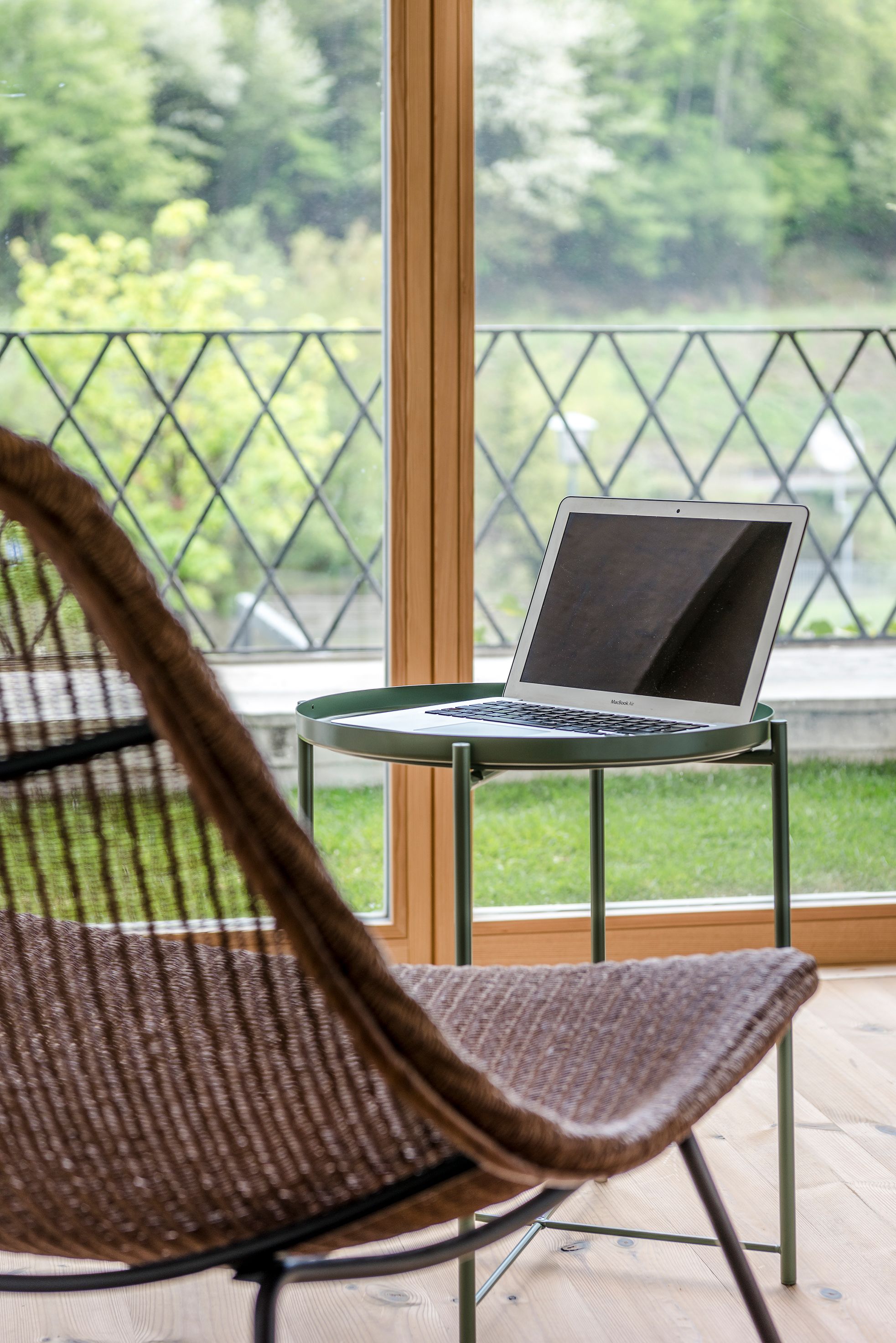 Ein Laptop steht auf einem kleinen Tisch, im Hintergrund ist durch ein Fenster grüße Vegetation zu sehen.