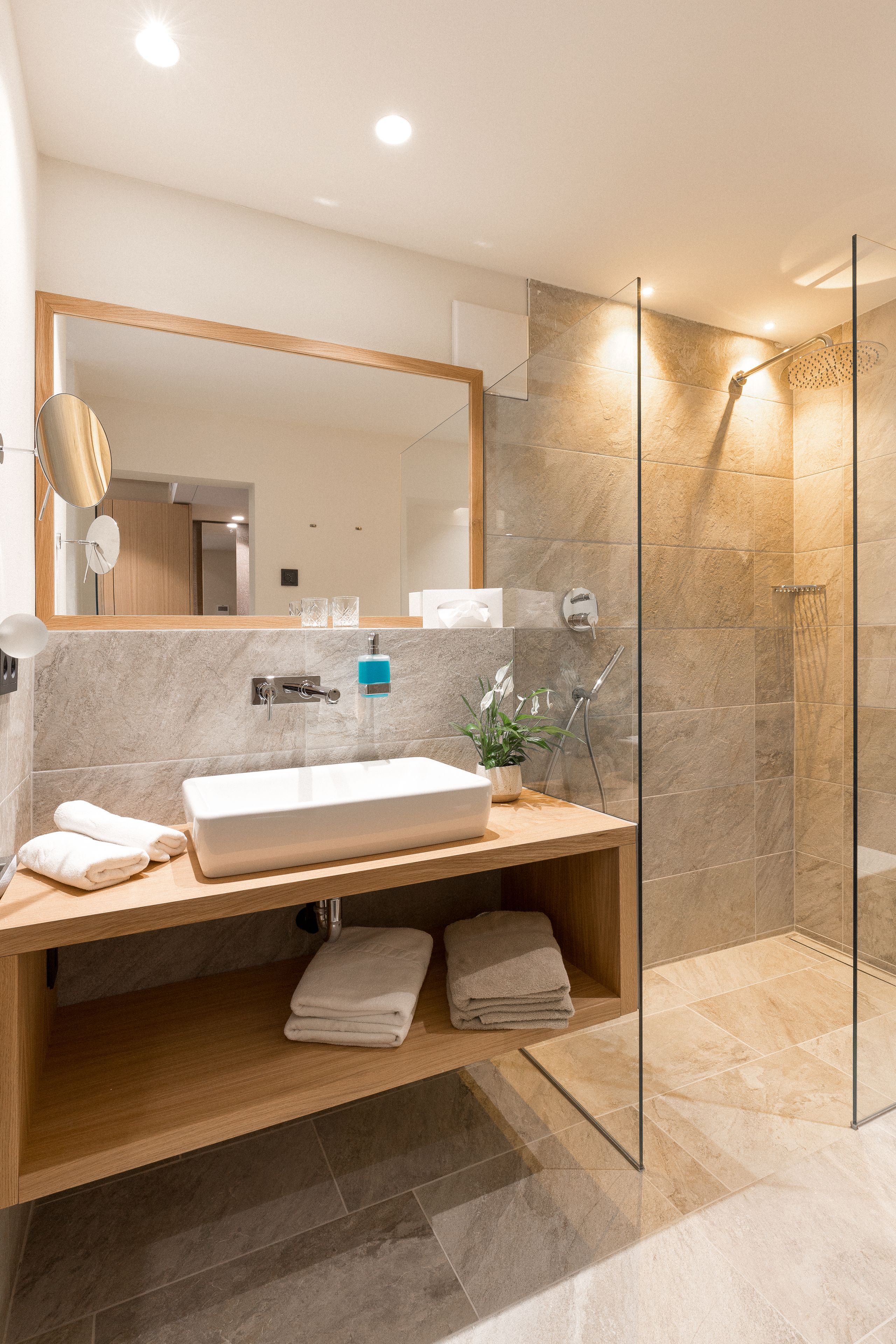 Een moderne badkamer met een grote spiegel, een wastafel, een douche met glazen wanden en een houten opbergmeubel.