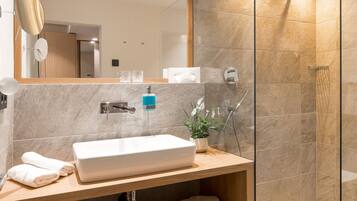 Een moderne badkamer met een grote spiegel, een wastafel, een douche met glazen wanden en een houten opbergmeubel.