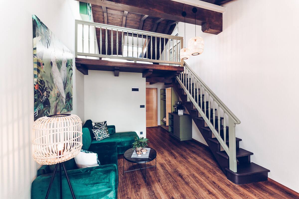 A spacious living area with a green sofa, a small round table, and a staircase leading to an upper level.