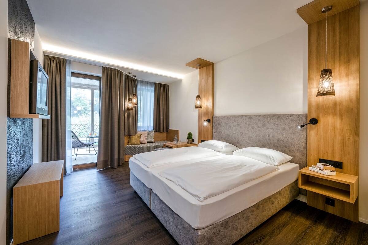 A modern hotel room with a large bed, a wooden bench, a small table, and a TV.