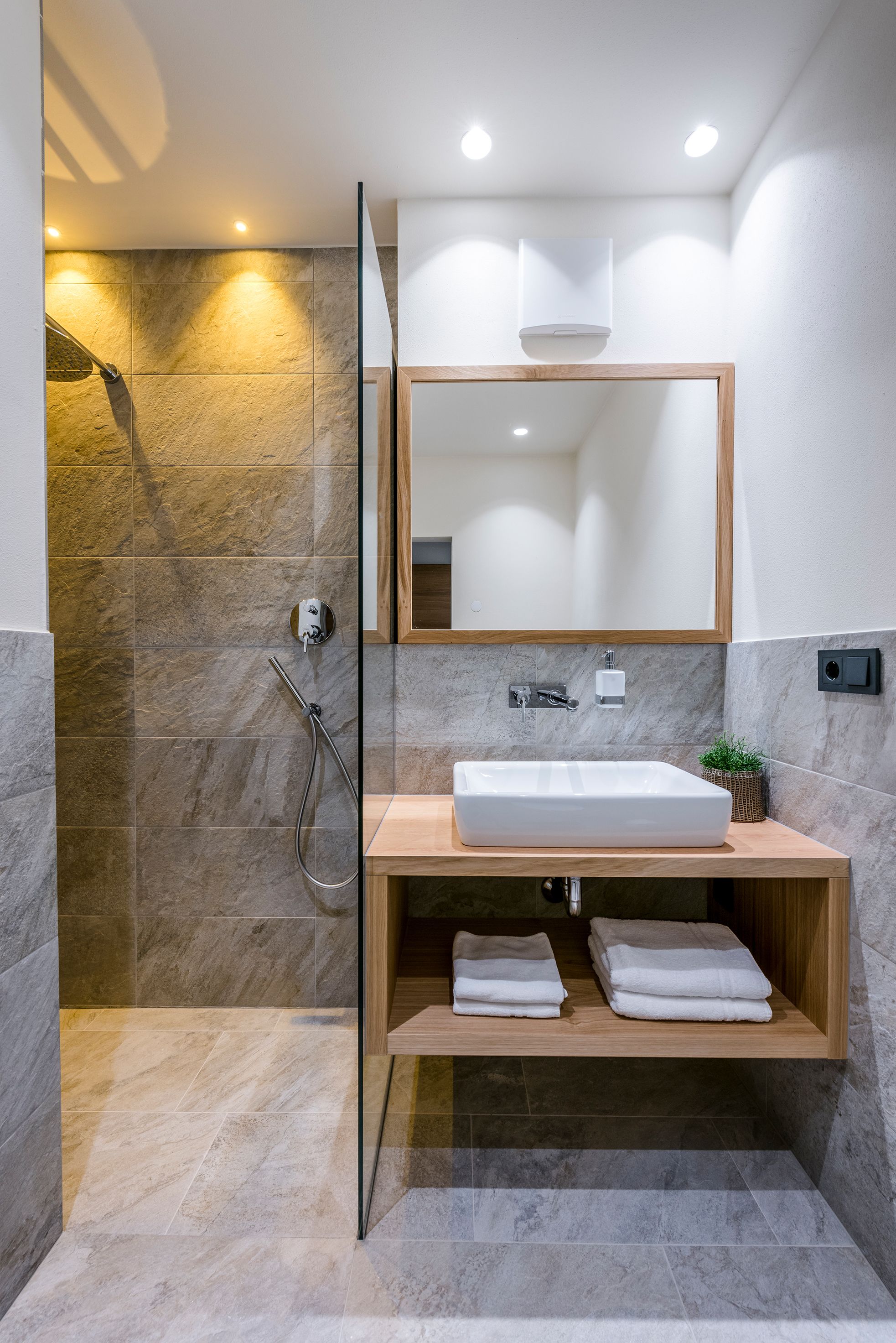 Une salle de bain moderne avec une douche à l’italienne en verre, un meuble-lavabo en bois avec un lavabo blanc et un miroir au-dessus.