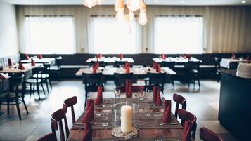 A restaurant with multiple tables set for dining, featuring a central candle centerpiece and red napkins.