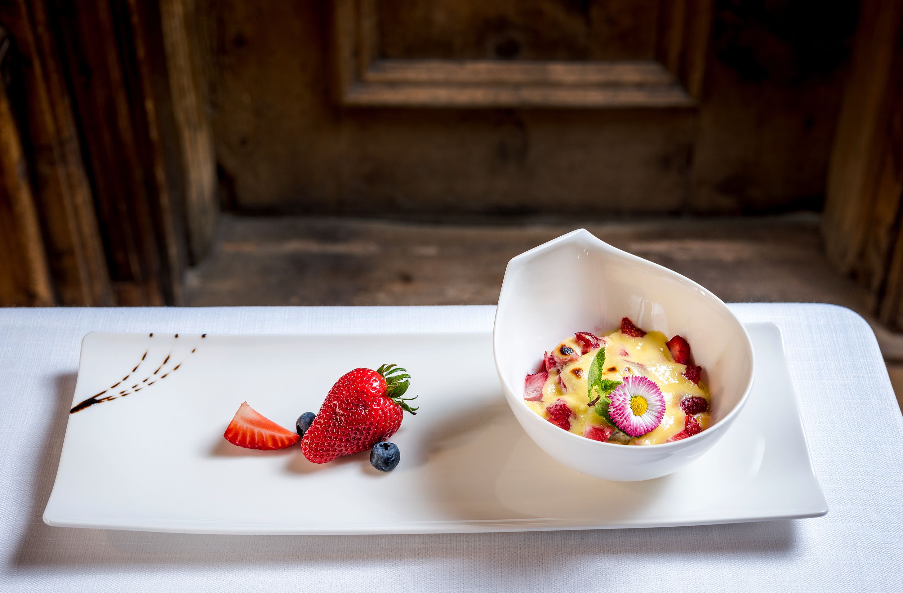 Ein Dessertteller mit Erdbeeren und Blaubeeren, sowie eine Schale mit Obstsalat und einer Zierblume.
