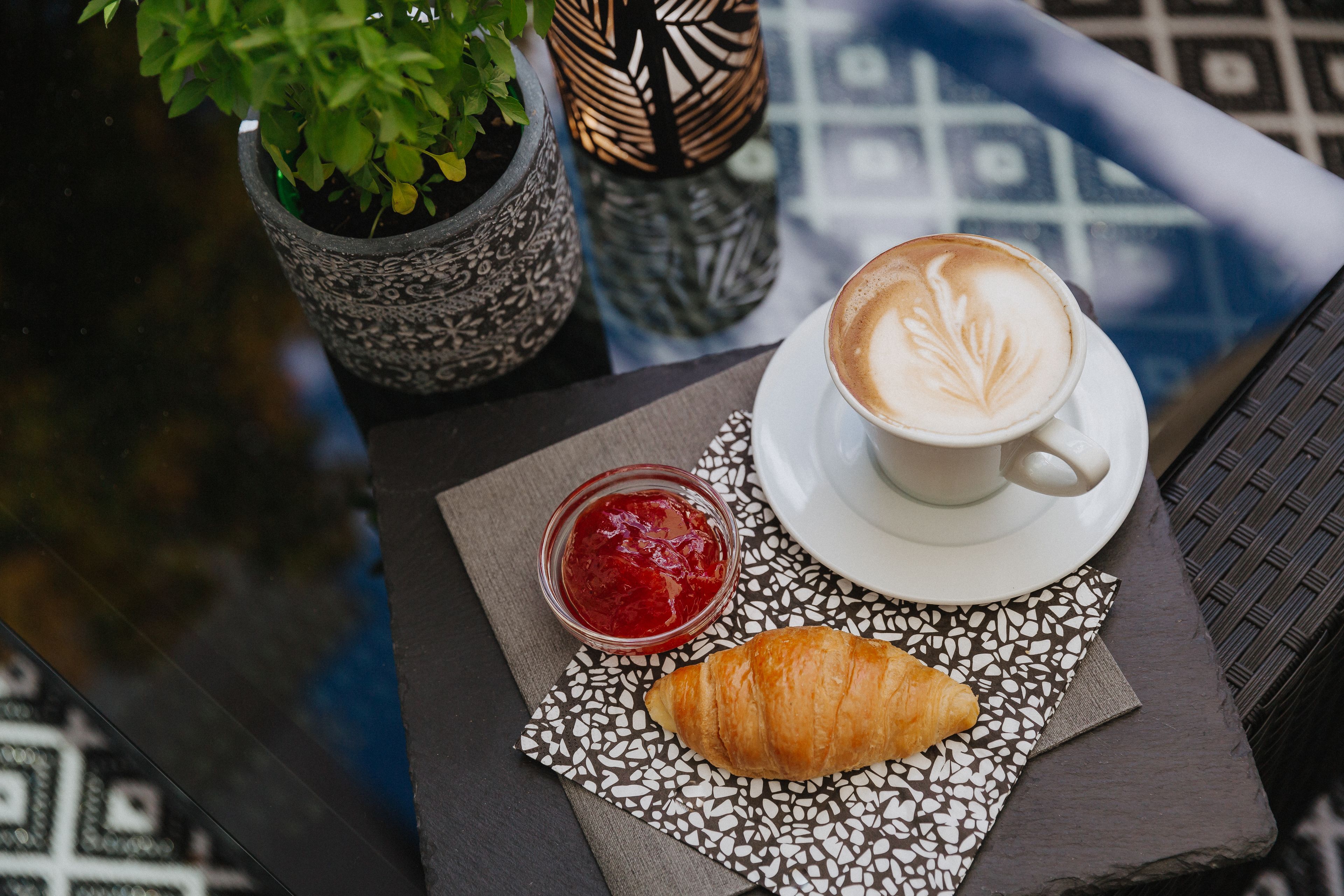 Une table avec un croissant, une tasse de café et un pot de confiture, le tout posé sur une serviette à motifs.
