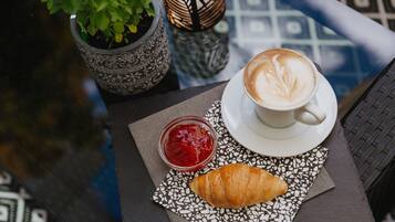 Une table avec un croissant, une tasse de café et un pot de confiture, le tout posé sur une serviette à motifs.