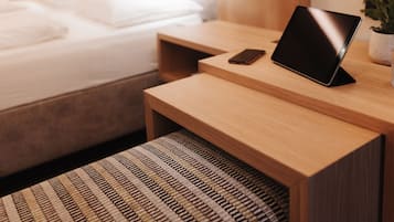 A neatly made bed with white linens, a bedside table with a smartphone and a tablet, and a small potted plant on the nightstand.