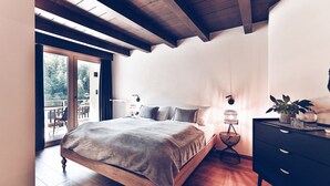 Een slaapkamer met een houten bed, een zwarte dressoir, een kleine tafel met een plant en uitzicht op de omgeving door een schuifdeur.