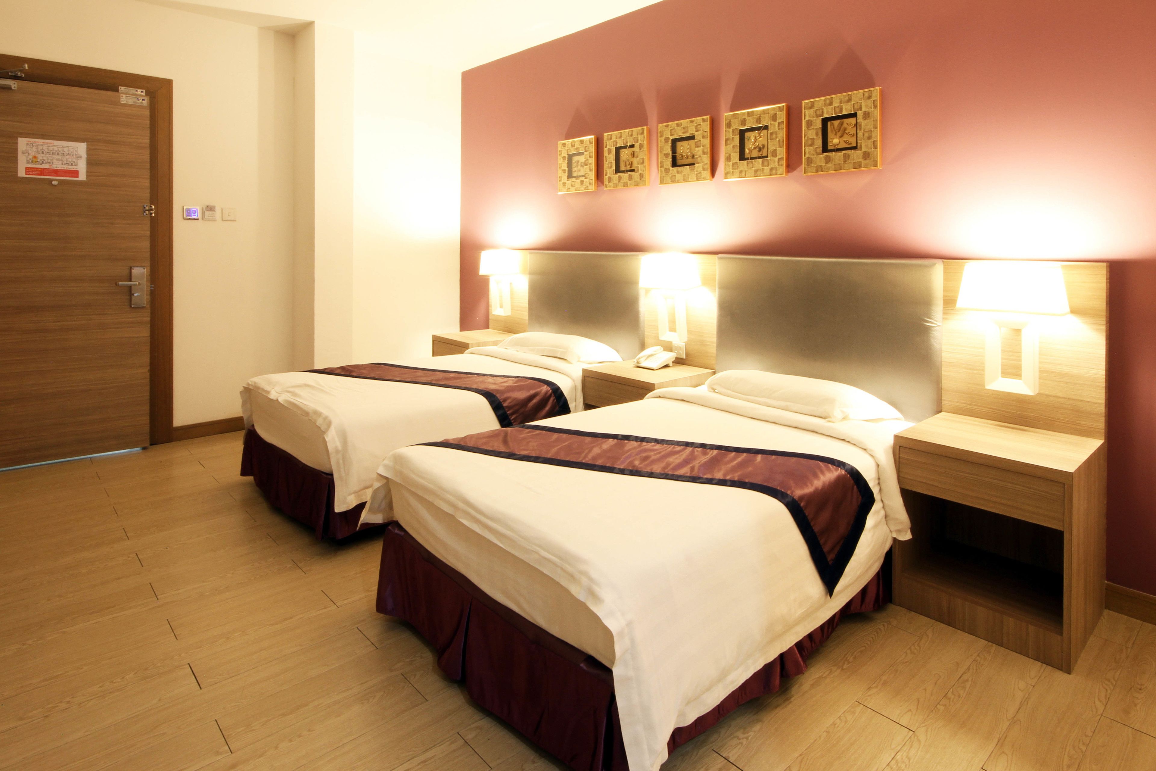 A hotel room with two beds, wooden floors, and a wall with three framed letters.