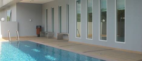 A modern indoor swimming pool with clear blue water, large windows, and a clean, minimalist design.