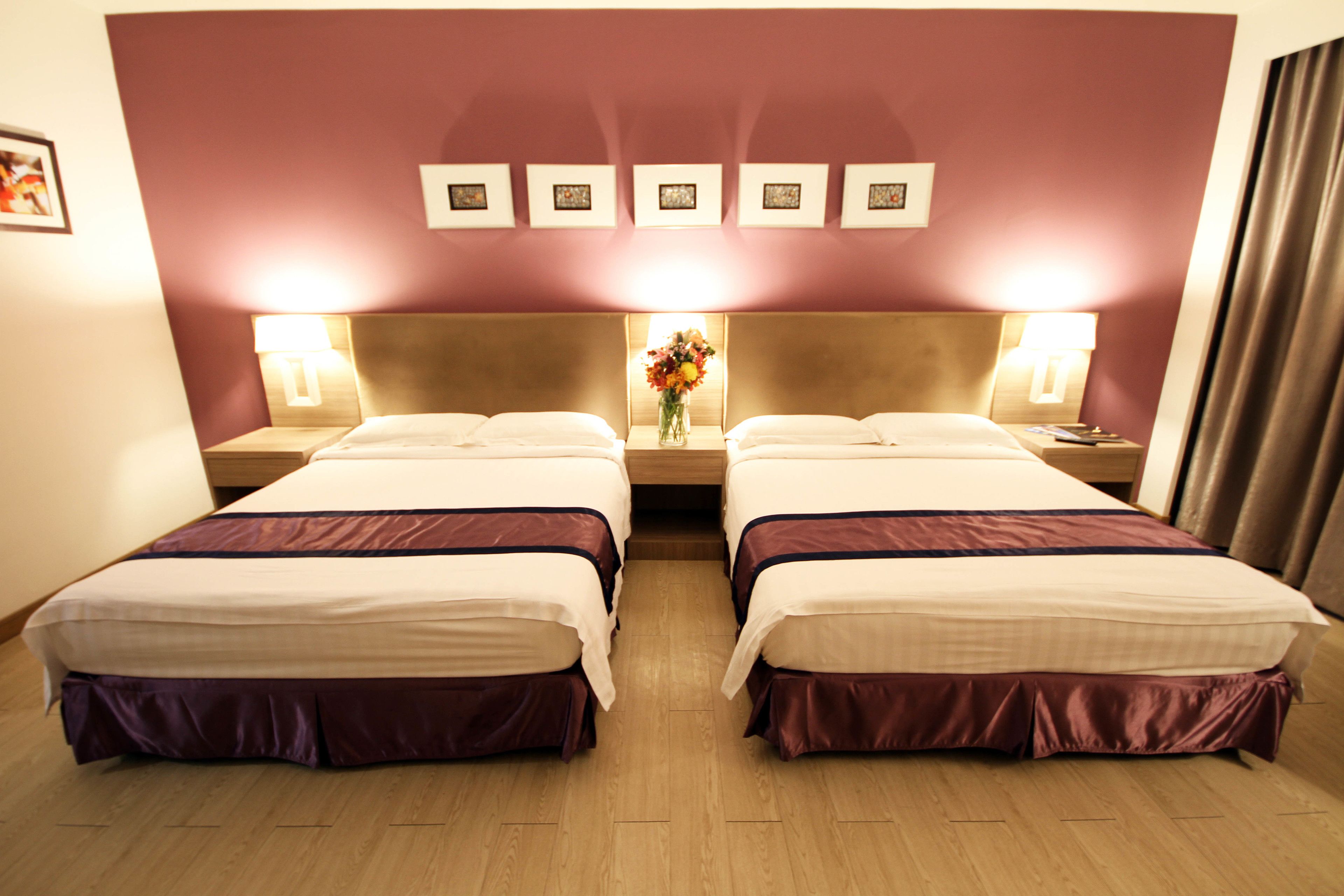 Een hotelkamer met twee bedden, een houten vloer en een muur met ingelijste foto's.