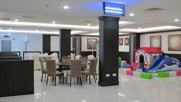 Un hall de hotel con zona de comedor, área de juegos infantiles y una televisión montada en un pilar.
