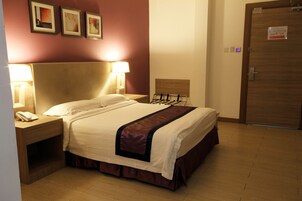 Habitación de hotel con cama, lámparas de noche, cabecera de madera, puerta de madera y teléfono instalado en la pared.