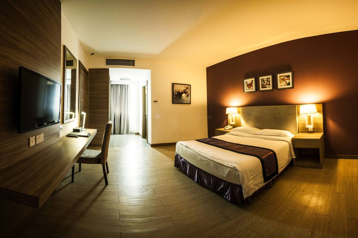 A hotel room with a bed, bedside tables with lamps, a desk with a TV, and a large mirror.
