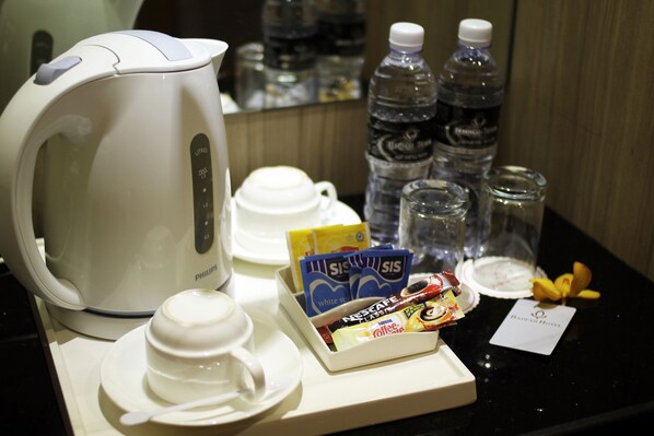 A coffee station with a Philips coffee maker, disposable cups, a box of Nescafe coffee, water bottles, and a tea bag.