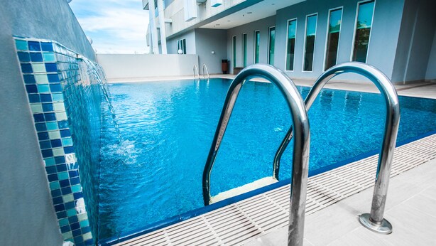 A modern indoor swimming pool with clear blue water, metal pool ladders, and a tiled edge. - Badi'ah Hotel (Bandar Seri Begawan)