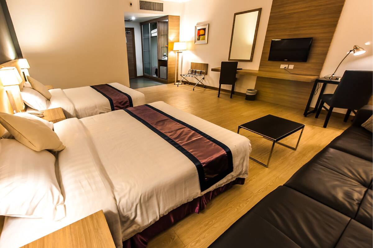 A hotel room with two beds, a desk, a chair, a TV, and a sofa.