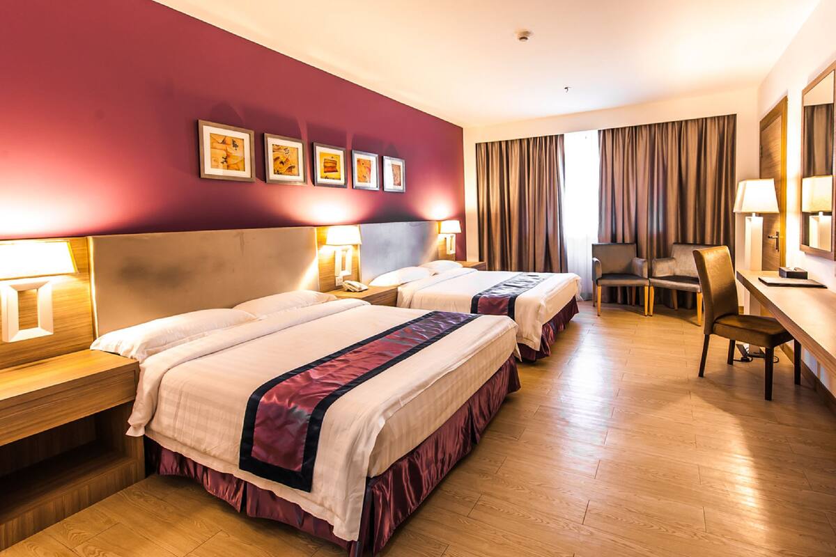 A hotel room with two beds, a desk, a chair, a TV, and artwork on the wall.