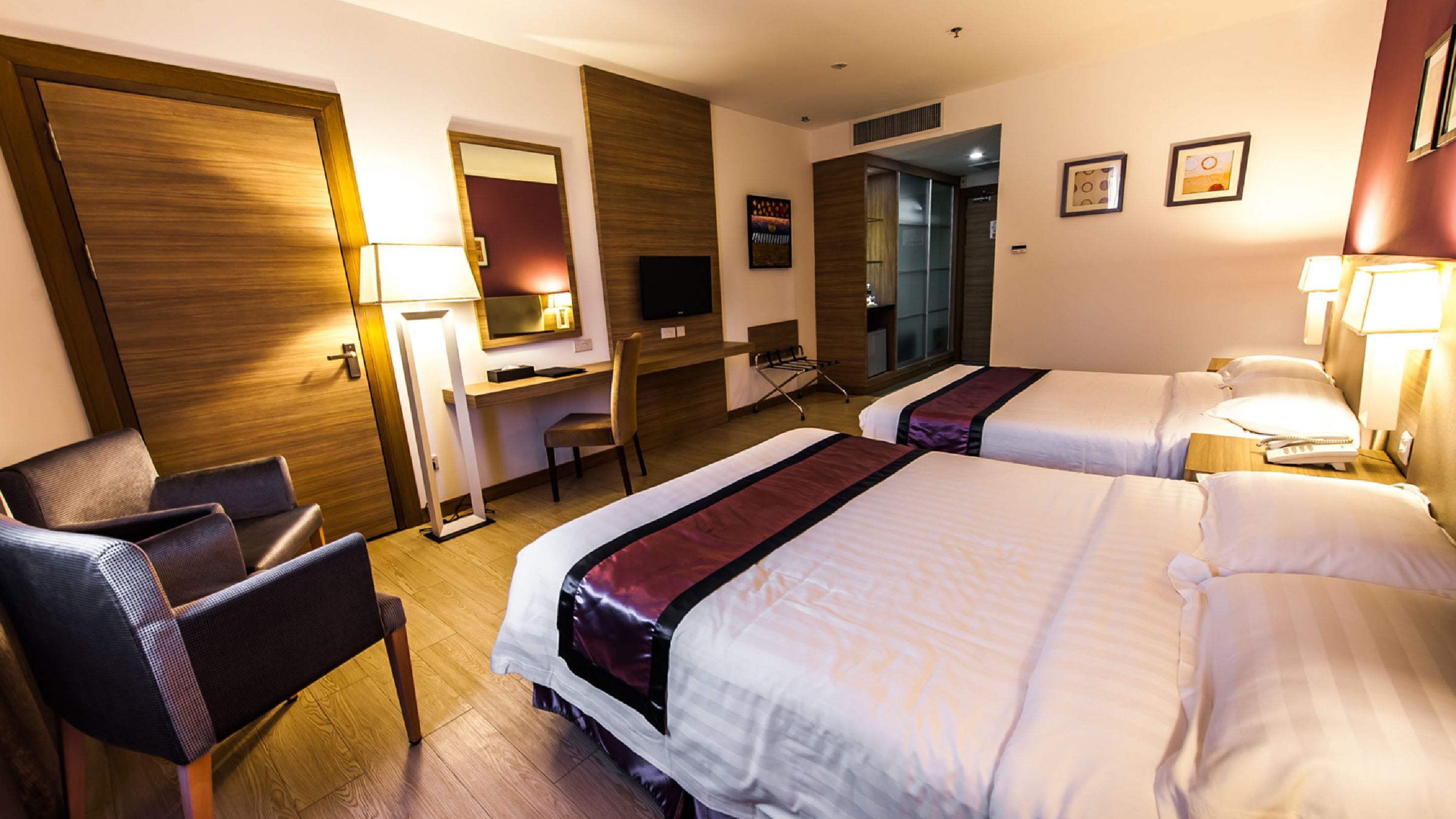 Ein Hotelzimmer mit zwei Betten, einem Schreibtisch, einem Stuhl, einem Fernseher und einem Spiegel.