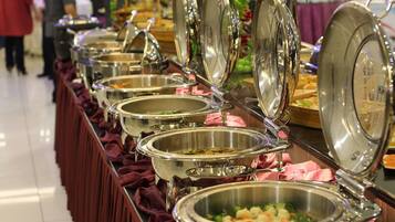 A buffet line with multiple stainless steel serving dishes, some with lids open, revealing food inside.