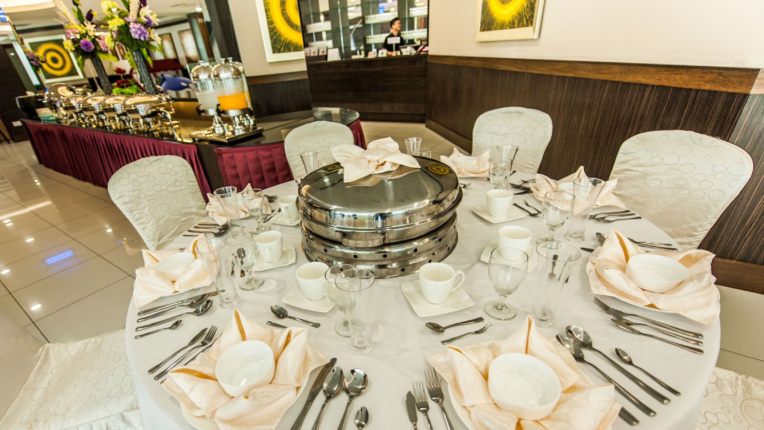 A round dining table set for a formal meal with white tablecloth, silverware, and glassware.