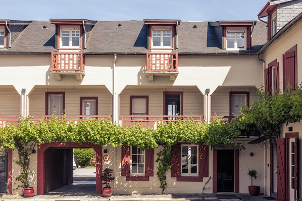 A row of traditional European-style buildings with red shutters and a covered walkway. - Le Clos du 5 - Appart Hotel Bagneres (Bagnères-de-Bigorre)
