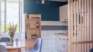 A modern kitchen with a wooden dining table, chairs, and a built-in bookshelf. - Le Clos du 5 - Appart Hotel Bagneres (Bagnères-de-Bigorre)