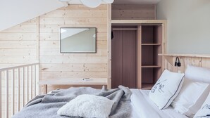 A bedroom with a wooden sloped ceiling, a bed with white and gray bedding, a bedside table, a mirror, and a wardrobe. - Le Clos du 5 - Appart Hotel Bagneres (Bagnères-de-Bigorre)