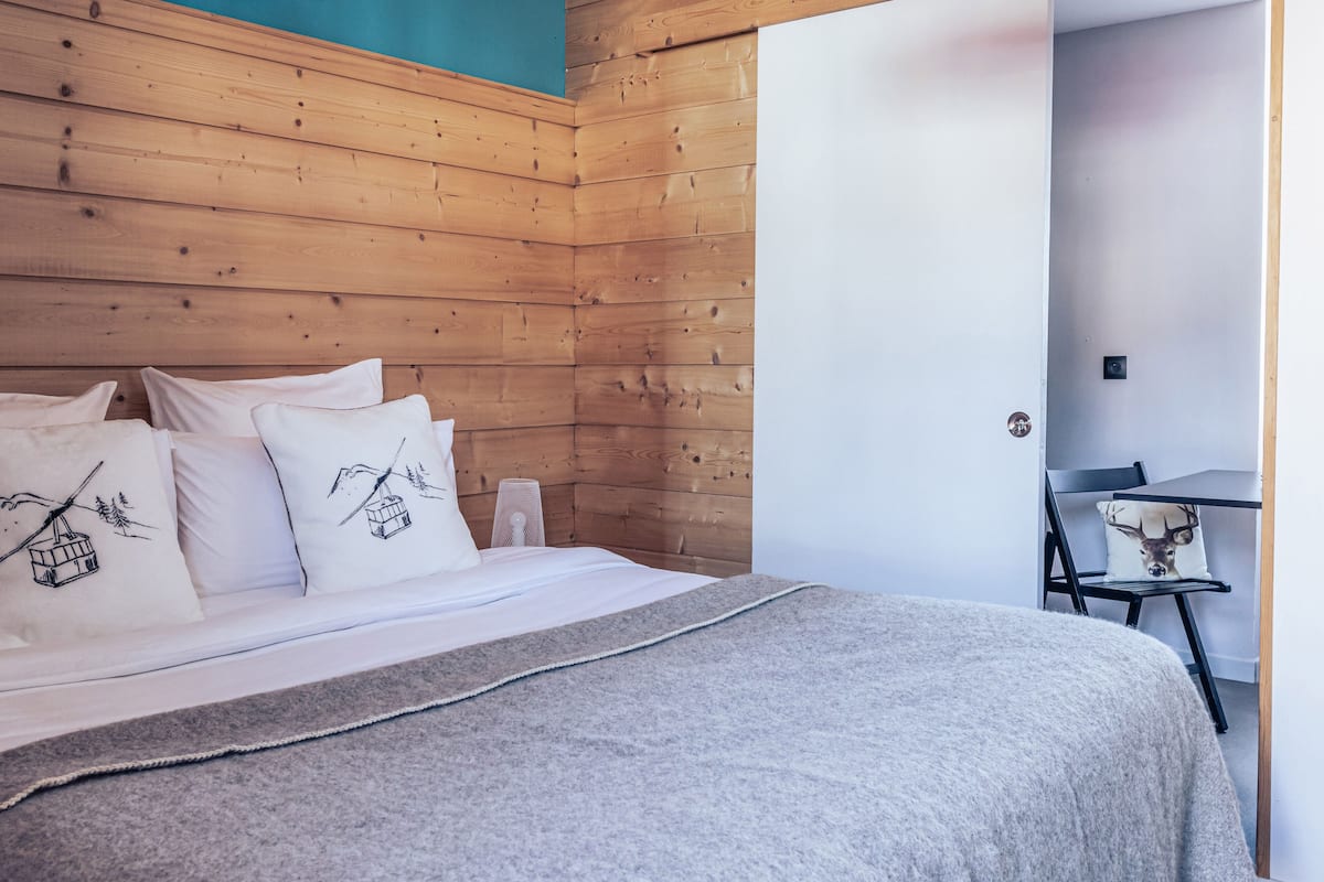 Ein ordentlich bezogenes Bett mit weißer Bettwäsche, dekorativen Kissen, einer grauen Decke und einem hölzernen Kopfteil.
