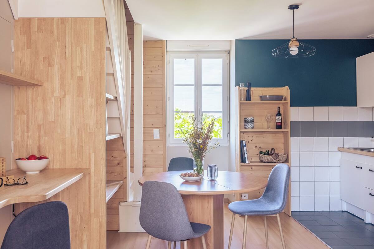 Eine moderne Küche mit Holdekor, einem Esstisch mit Stühlen, einer Vase mit Blumen und Blick durch ein großes Fenster.