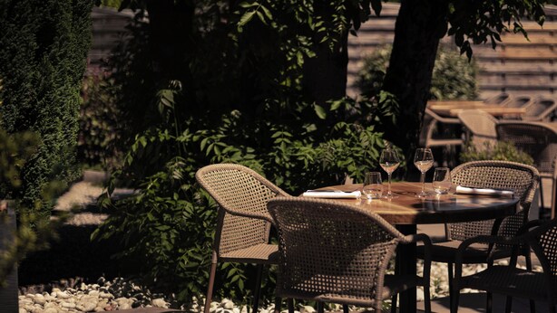 An outdoor dining area with wicker chairs and a wooden table, surrounded by greenery and a stone wall. - Le Clos du 5 - Appart Hotel Bagneres (Bagnères-de-Bigorre)