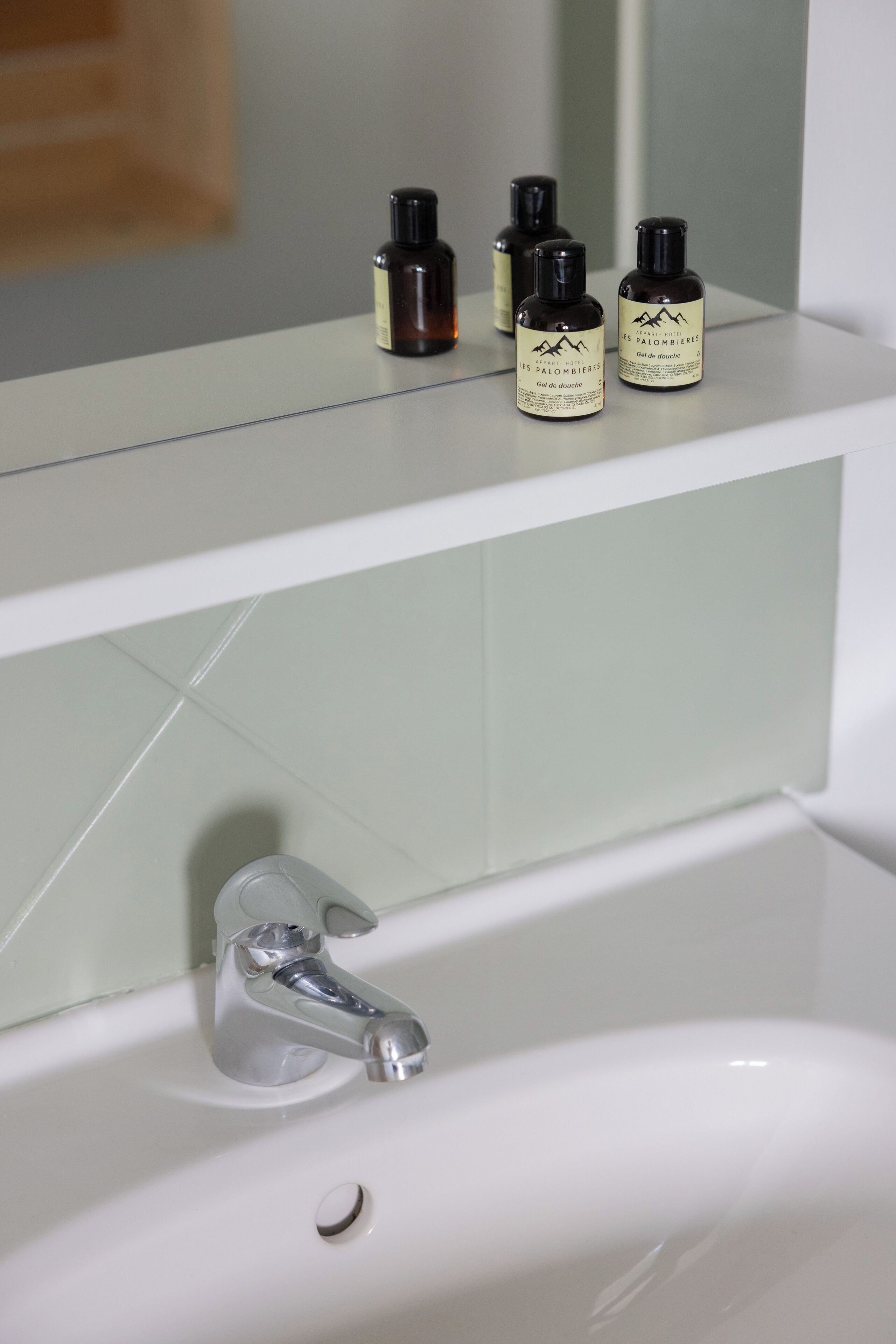 A bathroom with a white sink, a mirror, and three bottles of lotion on the countertop.
