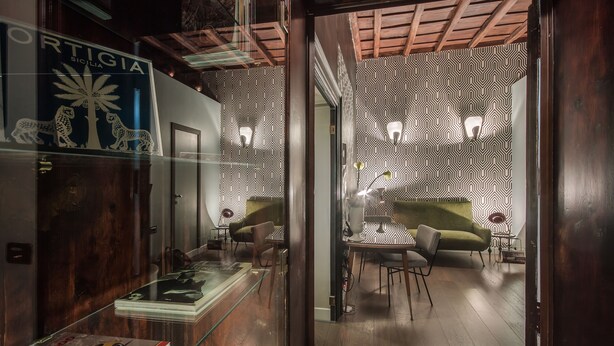 A modern interior with a patterned wall, a glass display case, and a dining area with a green sofa and chairs. - Frattina 57 (Rome)