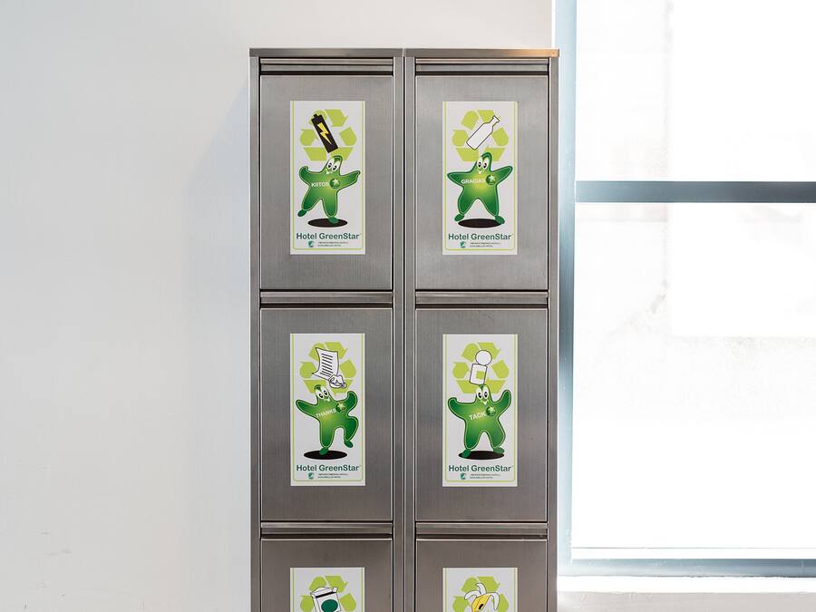 Ein Metallschrank mit Recyclingbehältern, beschriftet mit „Hotel GreenStar“, und ein Schild darüber mit der Aufschrift „Parkplatz P“.